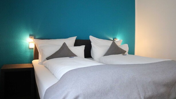 A neatly made bed with white bedding and gray pillows, a dark headboard, and teal walls.