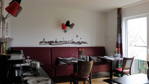 A dining area with a booth seating arrangement, a cityscape wall art, and a window with a view of trees.