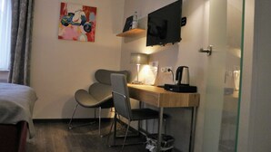 Et hotelværelse med en seng, et skrivebord med stol, et fjernsyn, en lampe og et billede på væggen.