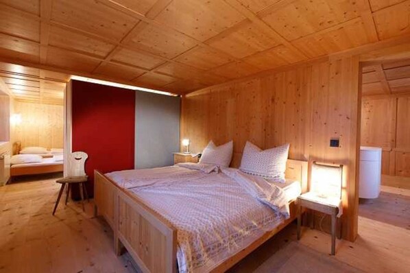 A wooden cabin bedroom with a bed, a chair, a nightstand, and a red wall. - Ferienwohnung Geser - Holiday flat/apartment (Egg)
