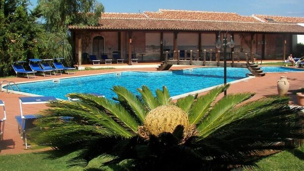 Uima-allas, jossa on aurinkotuoleja, katettu alue laattakatolla ja palmuja.