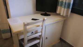Ein kleiner, weißer Schreibtisch mit Bildschirm, Stuhl und Schrank.