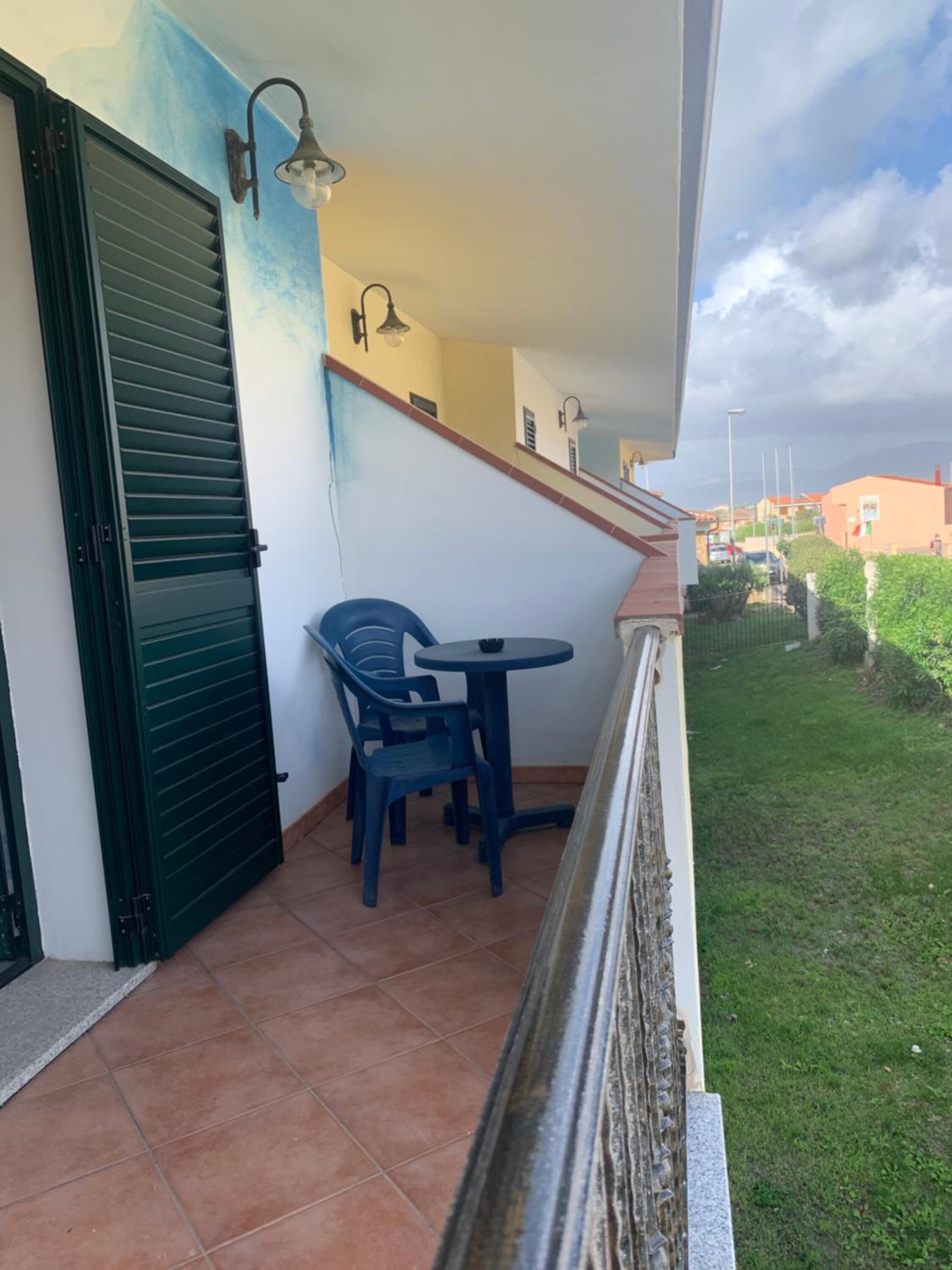 Un balcón con mesa y sillas, una puerta verde y vistas del barrio.
