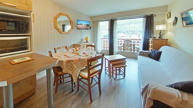 A compact room with a dining table, chairs, a sofa, a TV, and a balcony with outdoor furniture. - Charming Studio, Ski-In/Out, Sleeps 4, Balcony View, Parking, Near Village Center (Le Grand-Bornand)