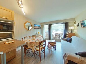 Une pièce de taille modeste comprenant une table à manger, des chaises, un canapé, un téléviseur et un balcon aménagé avec du mobilier d’extérieur.