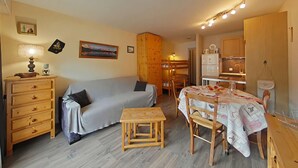 A compact living space with a sofa, a small wooden table, a dining table with chairs, a kitchen area, and a wooden wardrobe. - Charming Studio, Ski-In/Out, Sleeps 4, Balcony View, Parking, Near Village Center (Le Grand-Bornand)