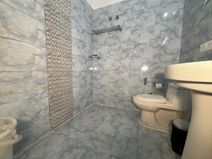 A bathroom with a shower, toilet, and sink, all with marble-like tiles. - Hotel Vedas Tapovan (Rishikesh)