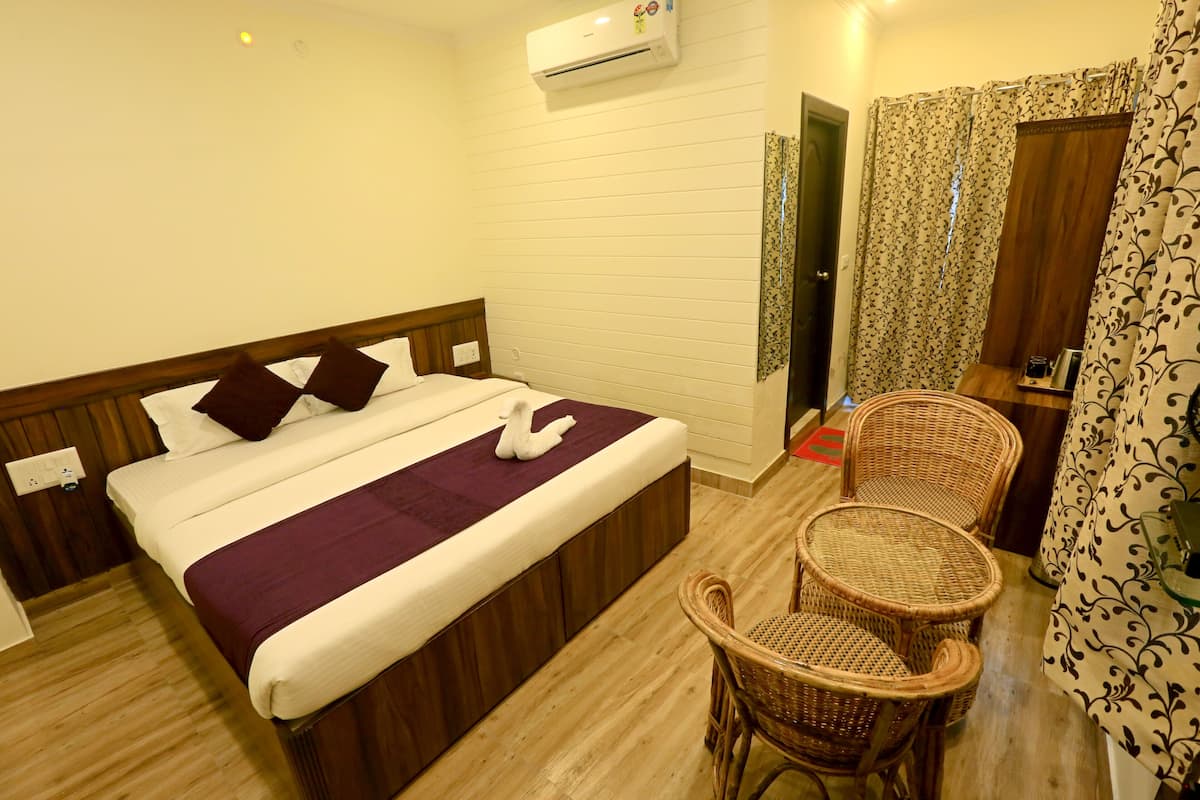 A hotel room with a bed, two wicker chairs, a small table, and a bathroom door.