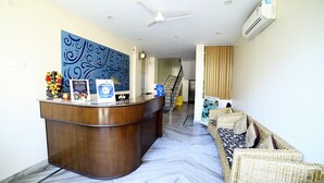 Un espace d’accueil avec un comptoir en bois, un grand mur décoratif, un ventilateur de plafond et un escalier menant à l’étage supérieur.