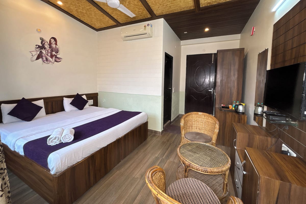 A hotel room with a bed, a ceiling fan, a television, a wicker chair, and a small table.