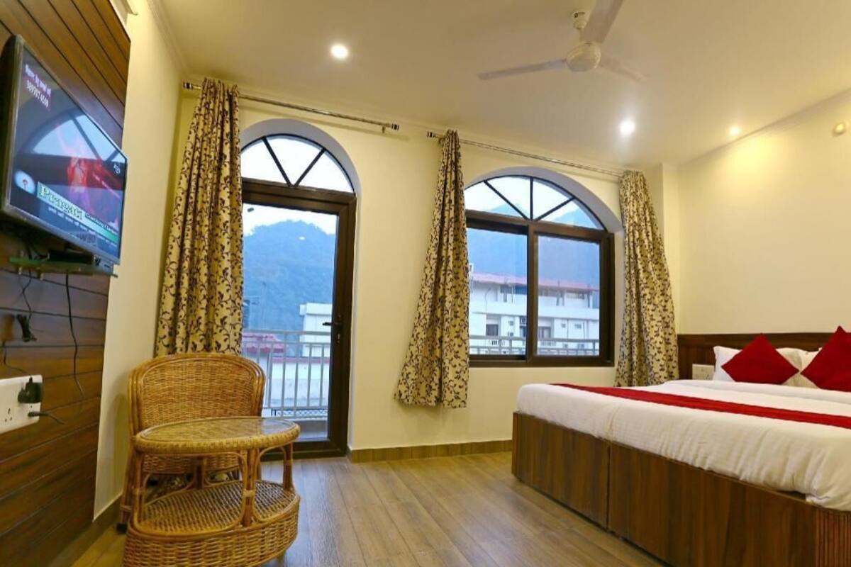 A hotel room with a bed, a chair, a TV, and large windows with curtains.