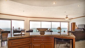 Een ruime keuken met een groot eiland, een vaatwasser en uitzicht op de oceaan door grote ramen.