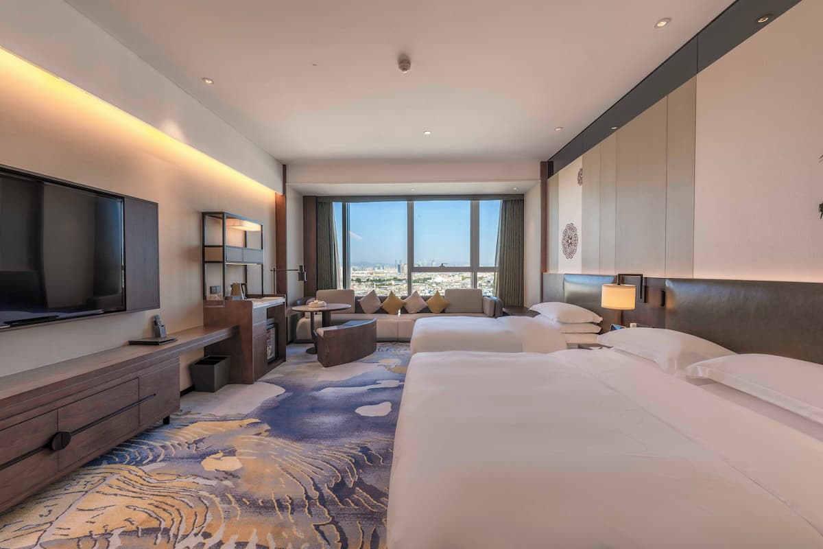 A hotel room with a large bed, a TV, a desk with a chair, a sofa, and a view of the city.