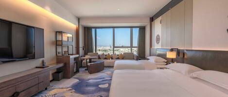 Habitación de hotel con una cama grande, televisión, escritorio con silla, sofá y vistas a la ciudad.