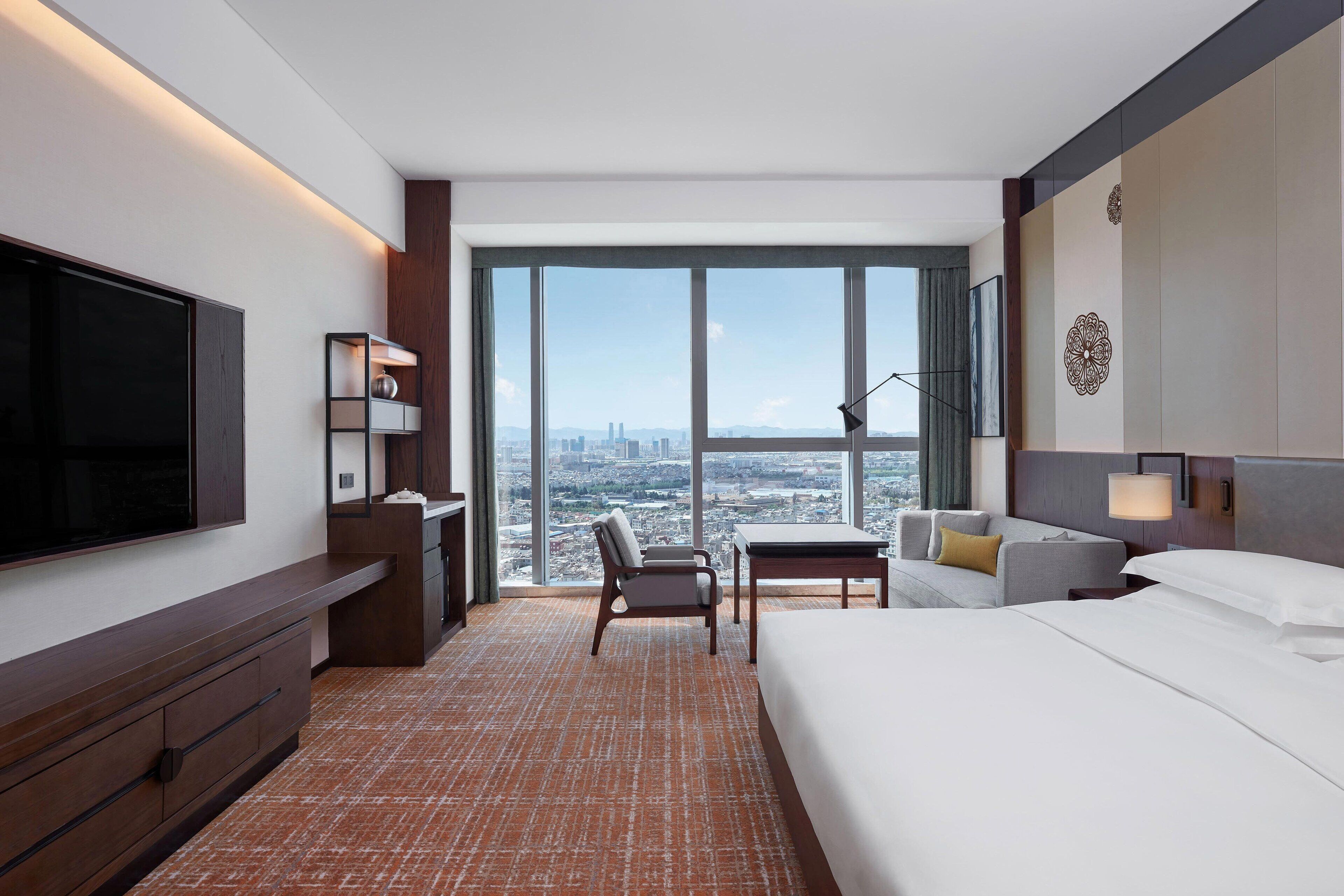 Habitación de hotel con una cama grande, un escritorio, una silla, un televisor y vistas a la ciudad.