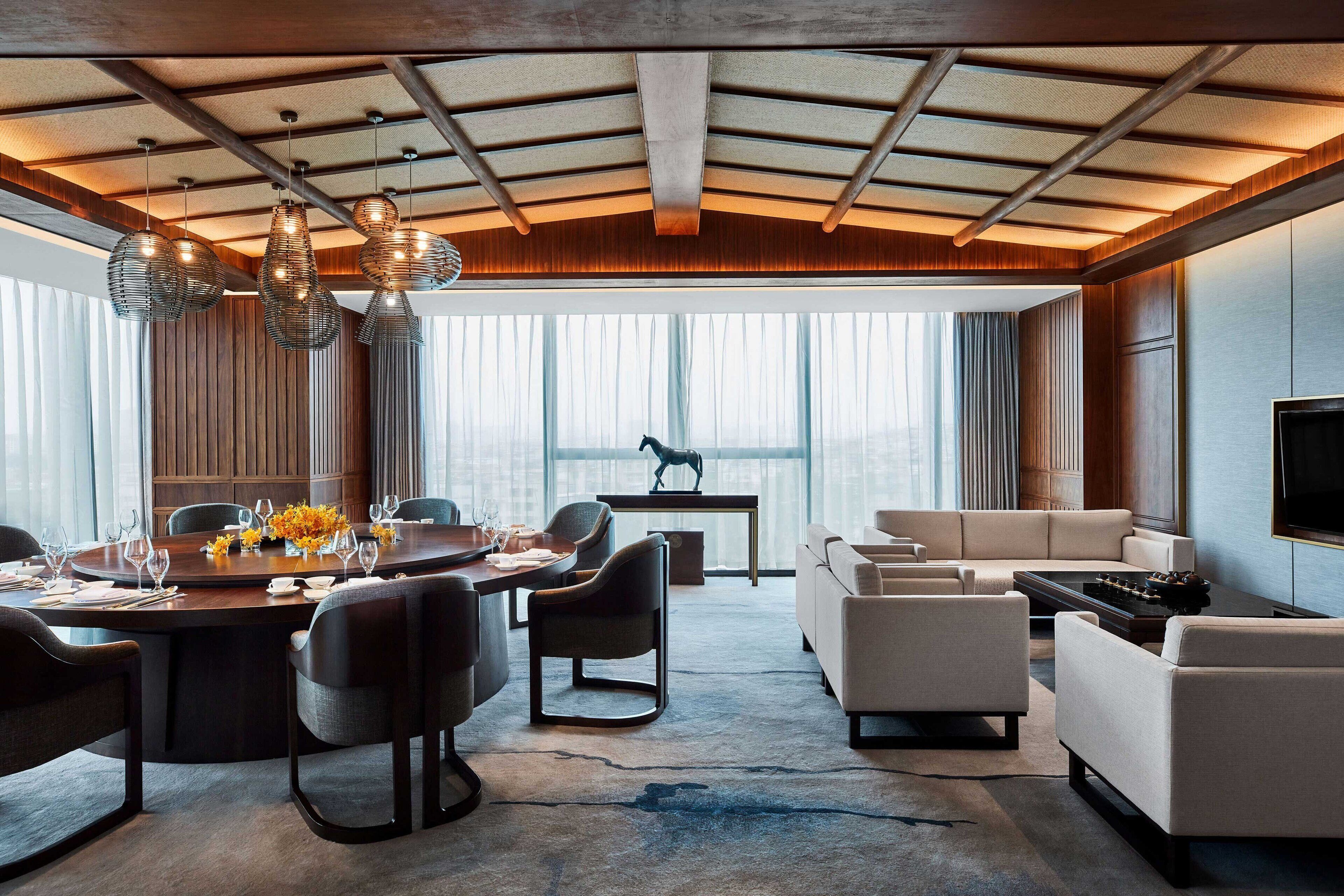A modern living room with a dining area, large windows, and a flat-screen TV.