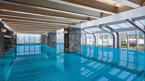 Une piscine intérieure moderne, dotée de grandes baies vitrées offrant une vue dégagée sur le paysage urbain.