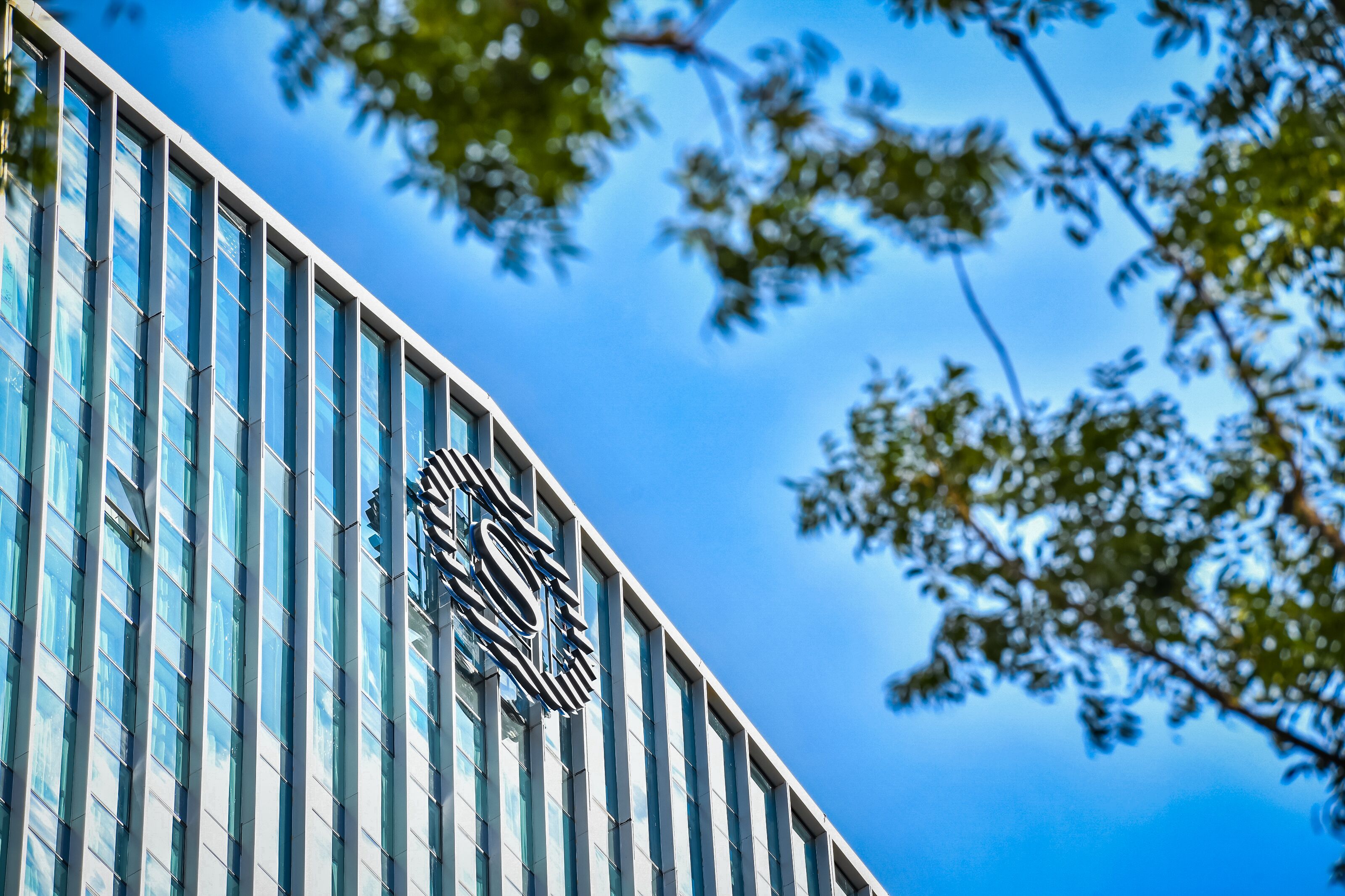 A modern building with a distinctive logo on its facade, large windows, and a clear blue sky in the background.