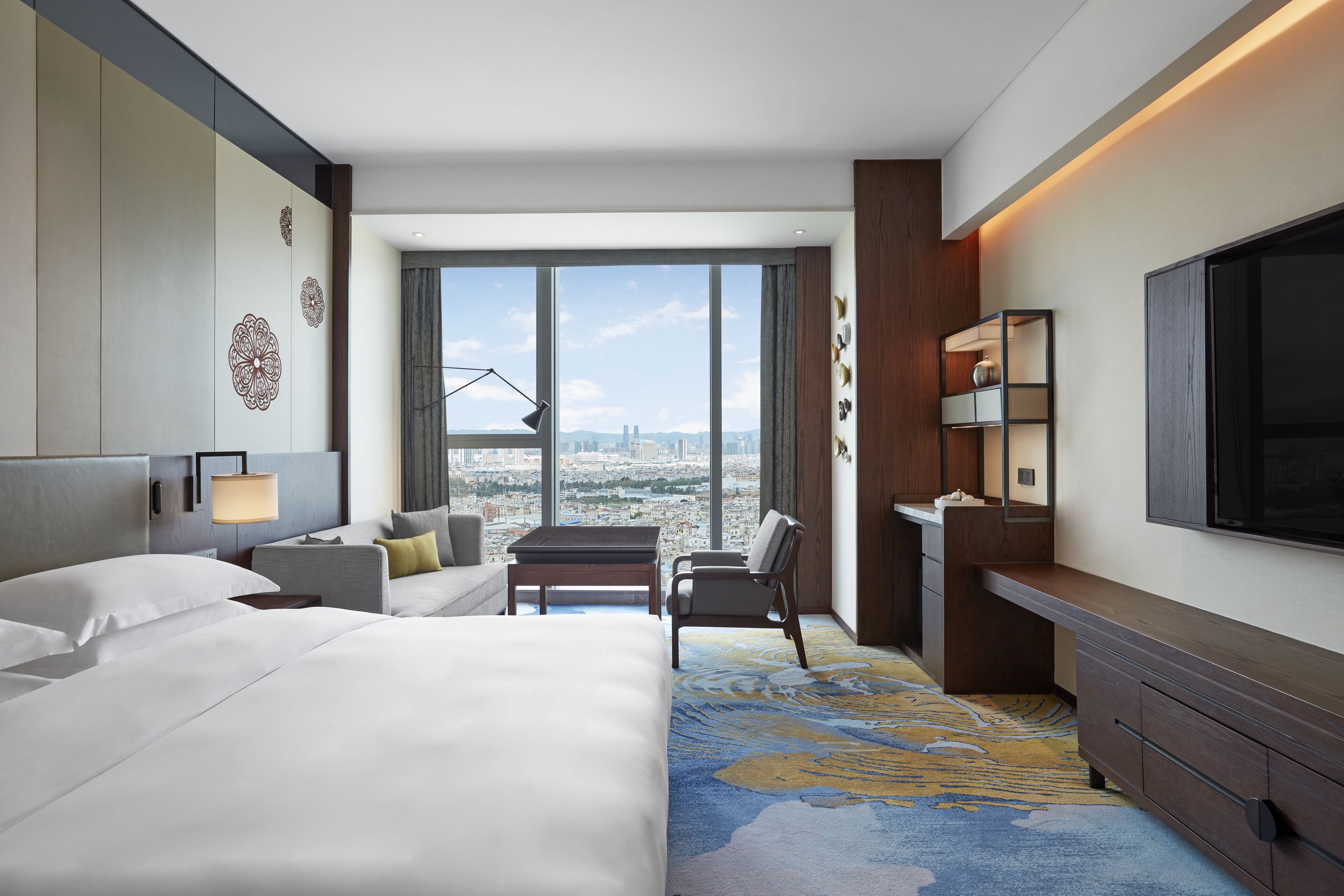 Una habitación de hotel con una cama grande, un escritorio, una silla, un televisor y vistas a la ciudad.