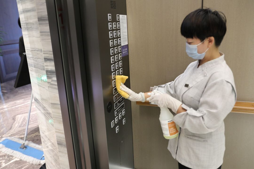 A person cleaning an elevator control panel with a mop and a cleaning spray bottle.