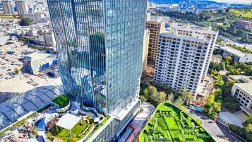 A high-rise building with a modern glass facade, surrounded by a well-maintained park and other buildings.