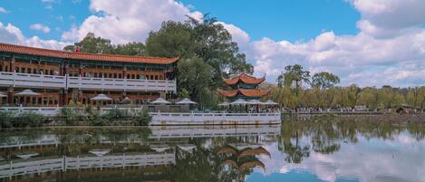 A traditional building with a reflection in a calm body of water, surrounded by trees and a clear sky.