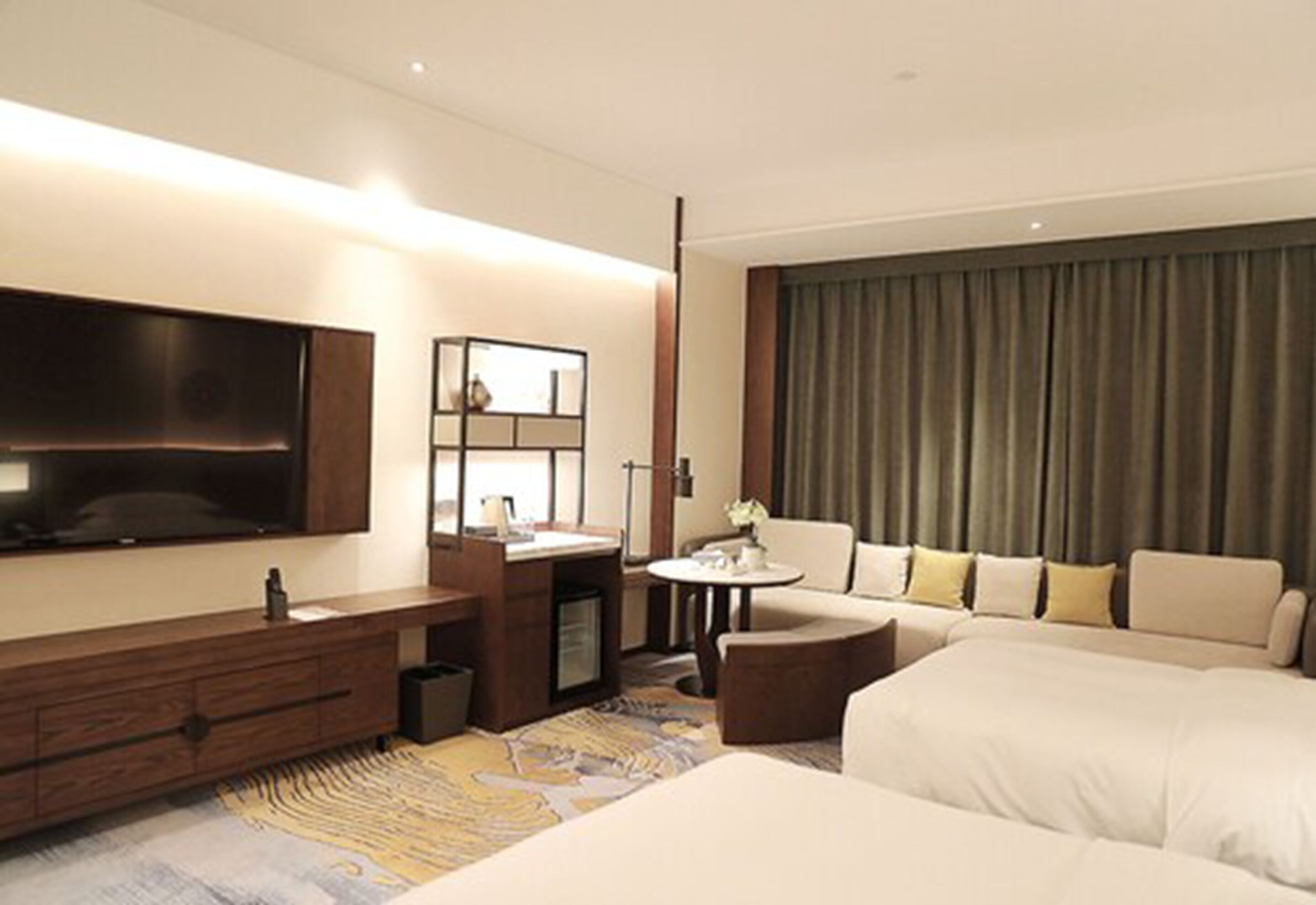 A modern hotel room with a large bed, a sofa, a TV, a desk, and a small table.