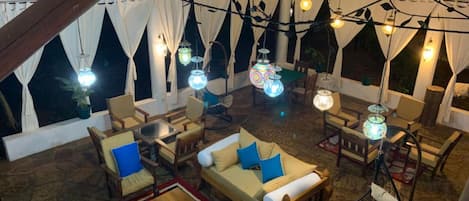 A cozy, well-lit indoor space with wooden furniture, a checkered rug, and string lights.