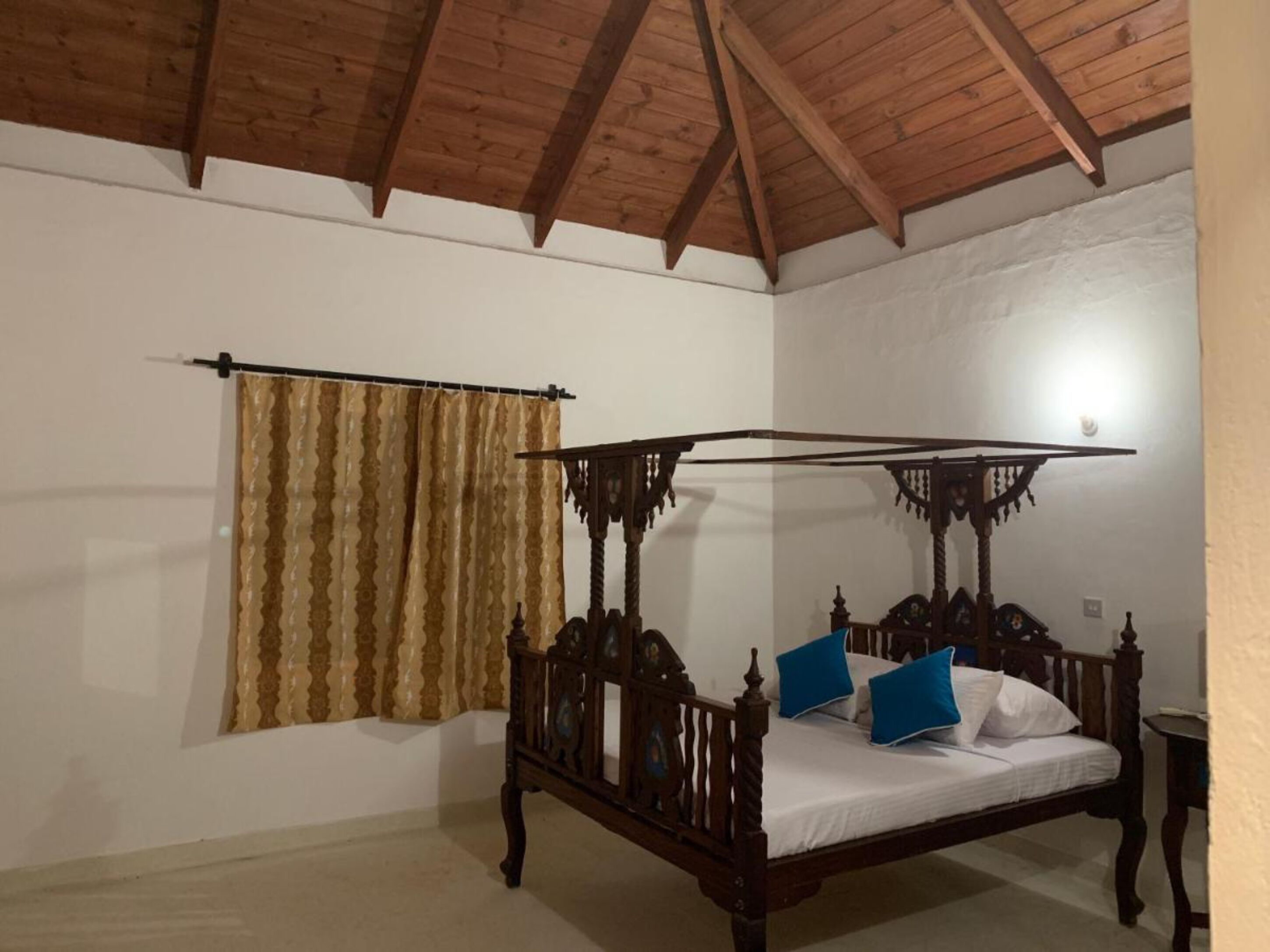 A four-poster bed with a canopy, a wooden ceiling, and a window with curtains.