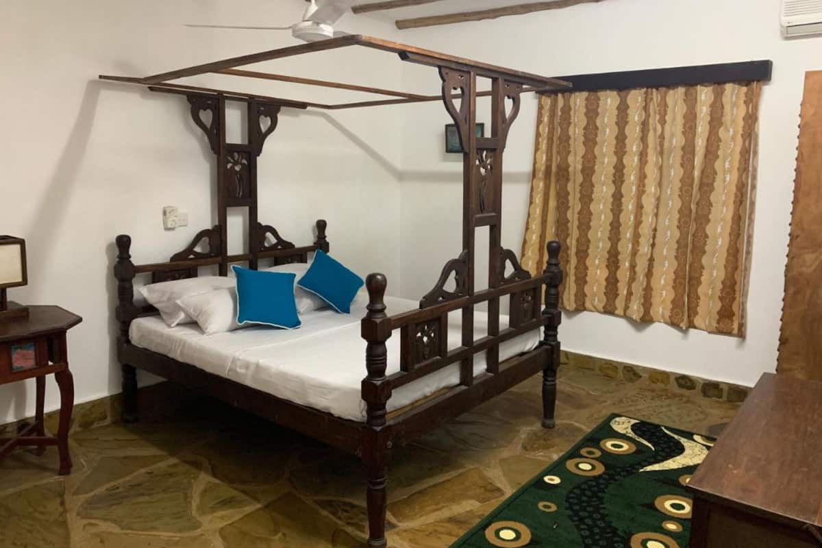 Una cama con dosel de madera, colchón blanco y dos almohadas azules.