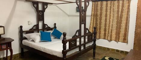 A four-poster bed with a wooden frame, a white mattress, and two blue pillows.