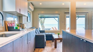 Eine moderne Küche mit Backofen, ein Essbereich mit Holztisch und Blick auf den Ozean durch große Fenster.