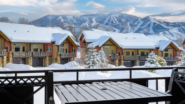 En rad hus i chaletstil med balkonger, med snötäckta berg som bakgrund.