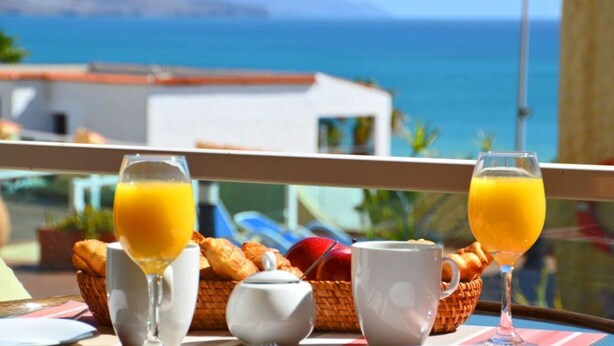Une table de petit-déjeuner avec des croissants, une théière et des verres de jus d’orange, donnant sur une vue sur la côte.