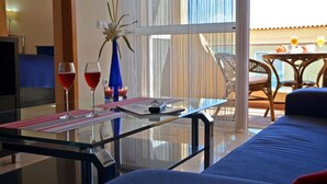 Une chambre d’hôtel avec une table en verre, deux boissons rouges, un vase avec des fleurs et une vue sur le balcon extérieur.