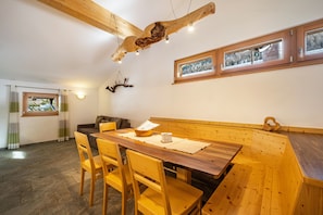 A dining area with a wooden table and chairs, a bench, and a wooden ceiling beam.