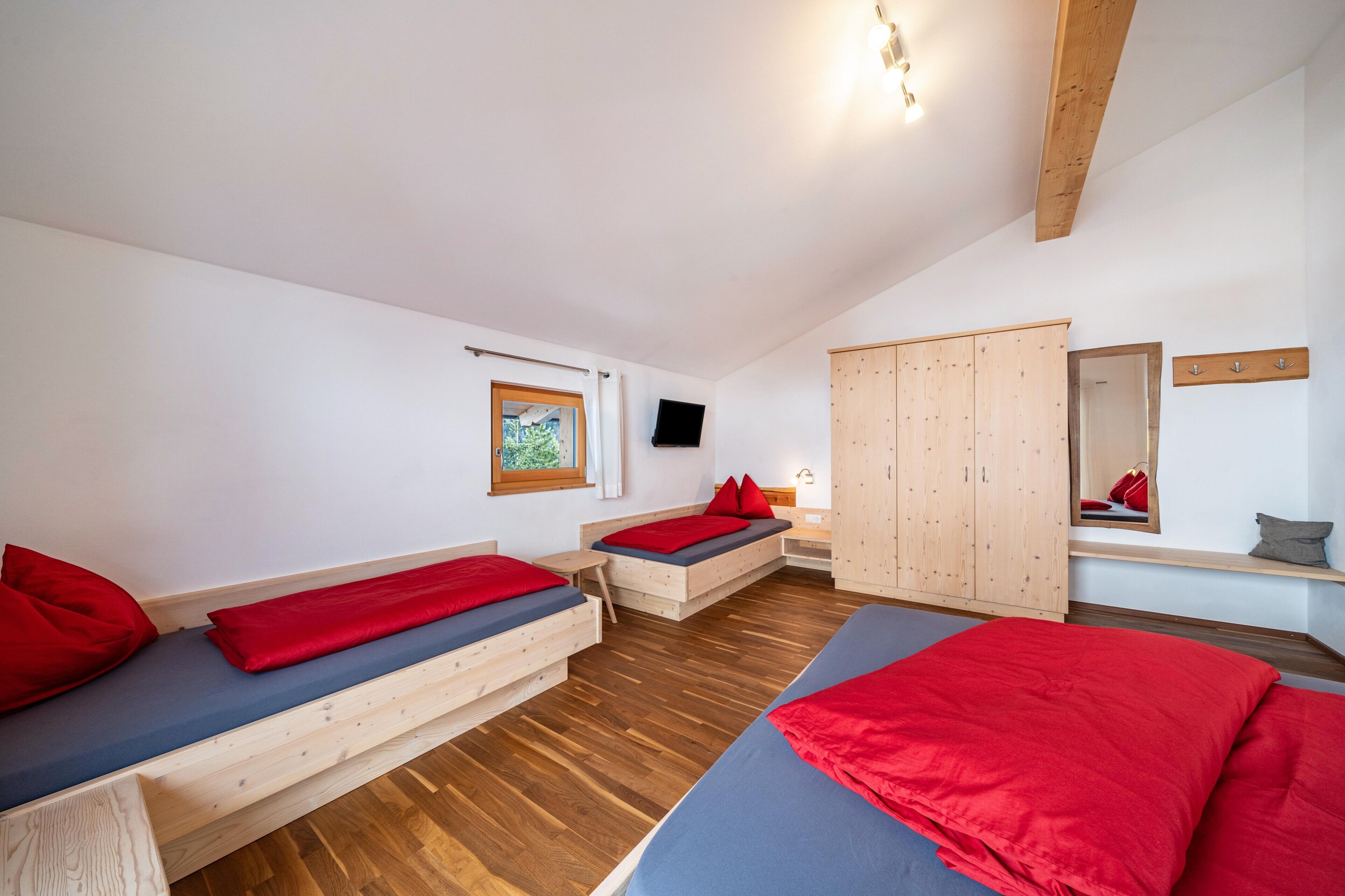 Een kamer met twee bedden, een houten garderobe, een televisie en een raam met gordijnen.