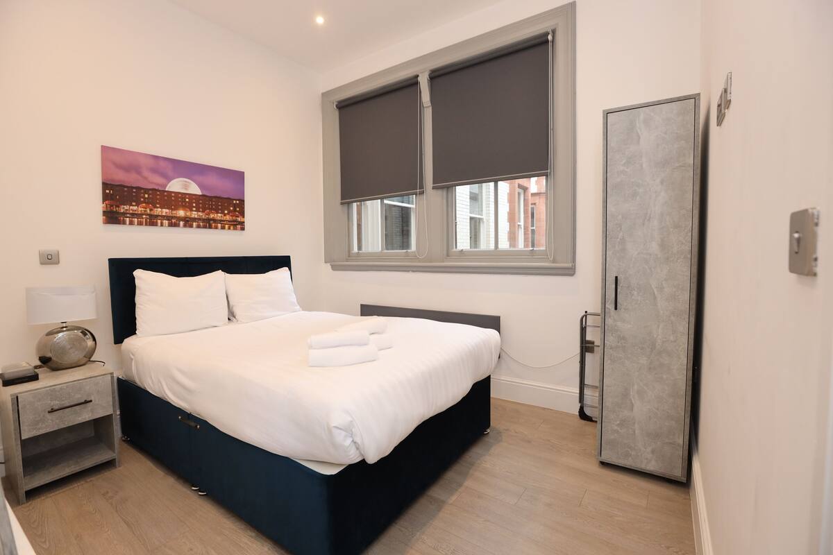 A neatly arranged bedroom with a bed, bedside table, lamp, and a painting on the wall.