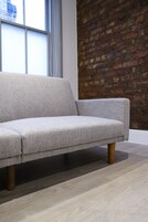 Un salón moderno con un sofá gris, patas de madera y una pared de ladrillo.