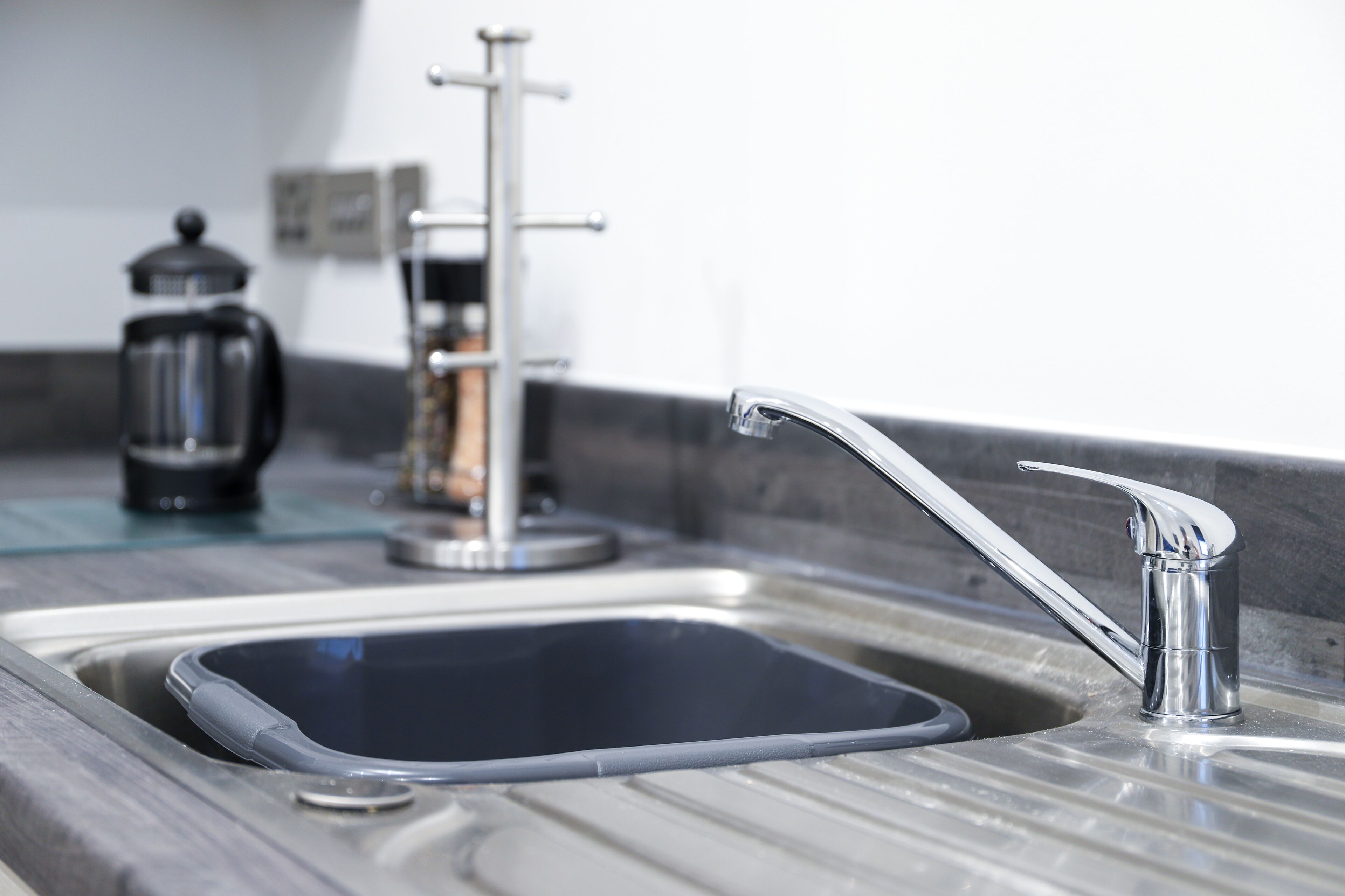 A modern kitchen sink with a chrome faucet, a coffee maker, and a glass container on the countertop.