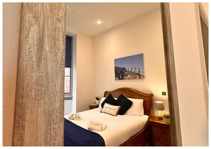 A neatly made bed with a headboard, a bedside lamp, a small table with a vase and a plant, and a framed picture on the wall. - 16 Queen Avenue (Liverpool)