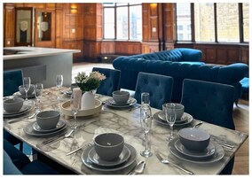 Un comedor con una mesa de mármol dispuesta para una comida, sillas tapizadas en azul y un jarrón con flores.