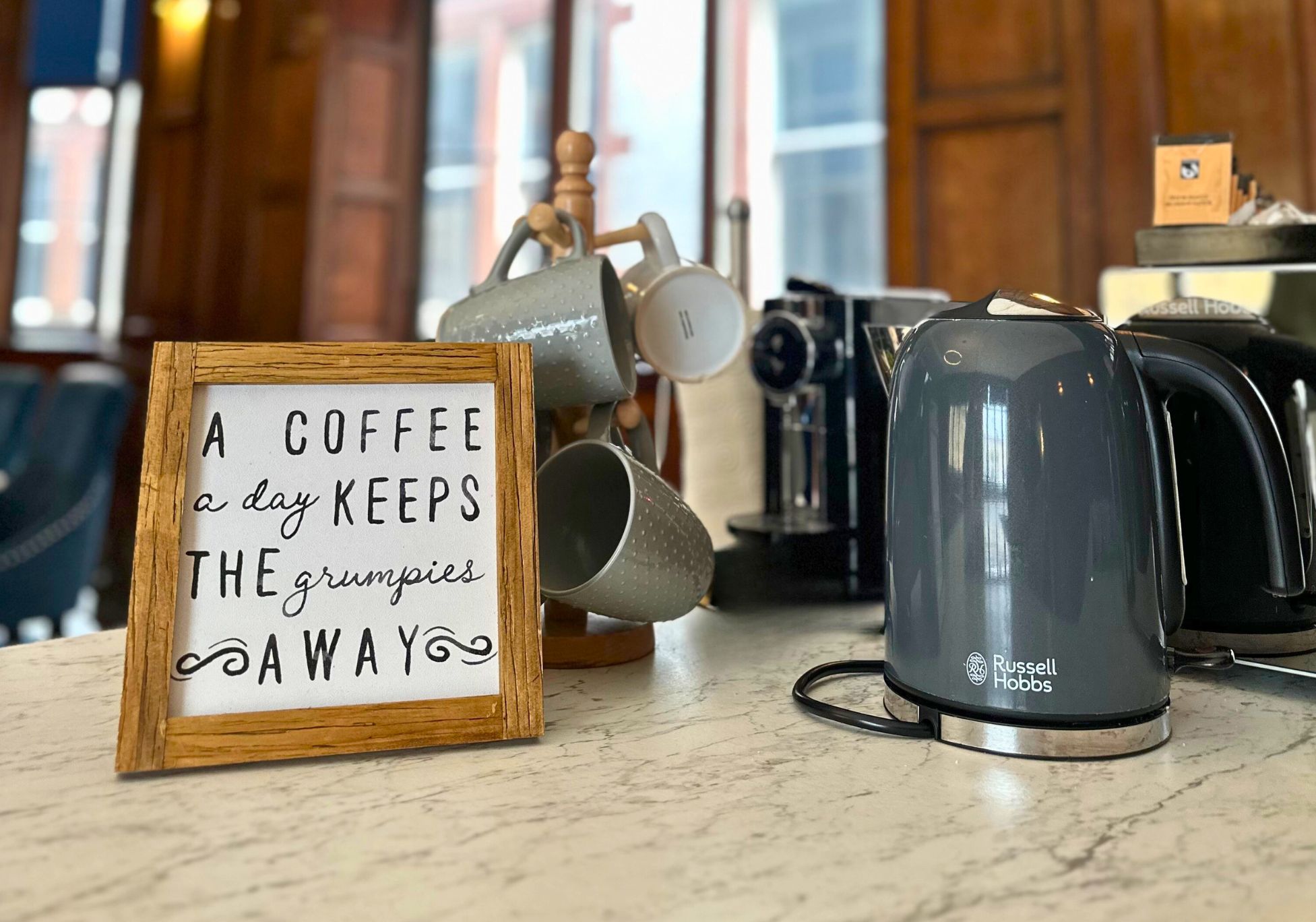 A kitchen counter with a coffee maker, a framed sign, and various kitchen items.