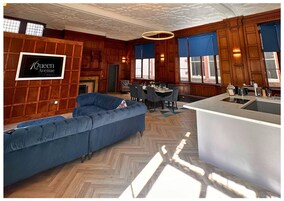 Un soggiorno moderno con un divano blu, una zona pranzo con tavolo e sedie, e una cucina con un piano di lavoro e lavello bianchi.