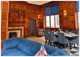 A room with a fireplace, wooden paneling, a dining table set for six, and a blue sofa.
