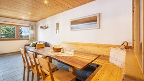 A wooden dining table with benches, a sofa, and a window with a view of trees. - Apartment "Enzian" on a Mountain Farm with Balcony (Moos in Passeier)