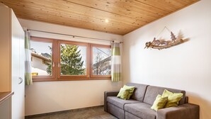 A room with a wooden ceiling, a sofa with pillows, a window with curtains, and a wall-mounted decoration. - Apartment "Enzian" on a Mountain Farm with Balcony (Moos in Passeier)