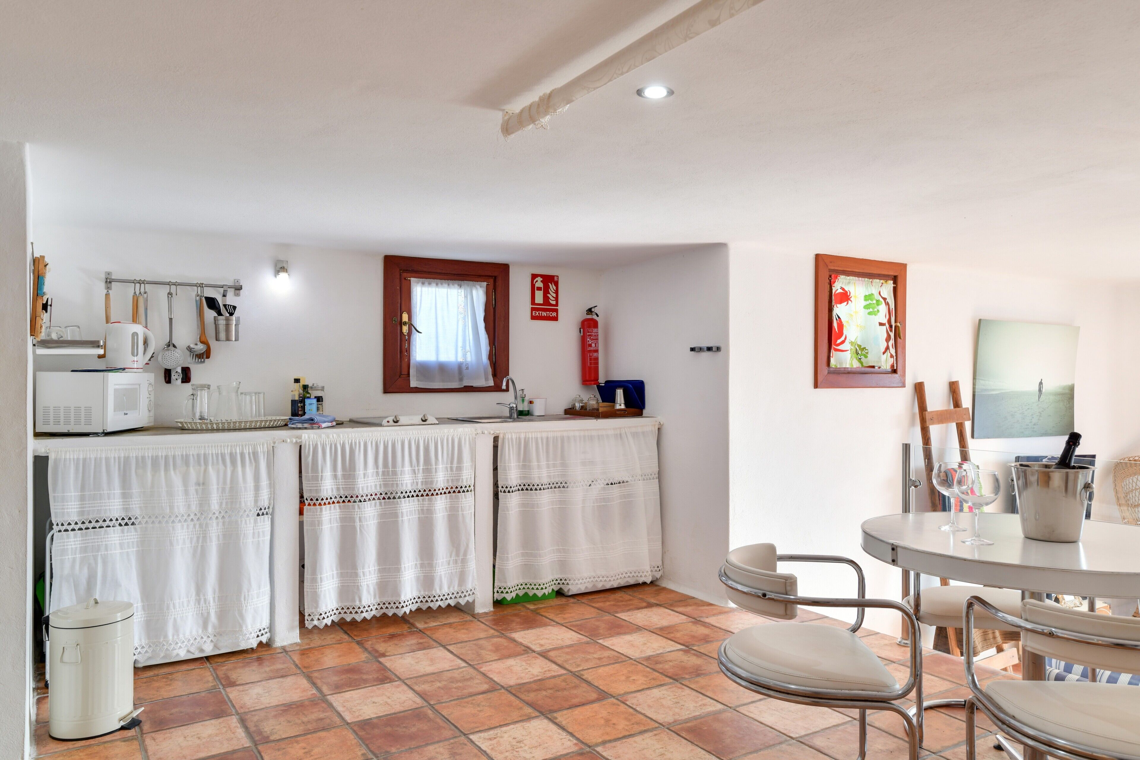 Une cuisine avec un sol carrelé, un évier, une cuisinière et une fenêtre avec des rideaux.