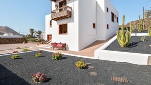 Un edificio moderno bianco con un balcone, una panchina rossa e cactus nel giardino.