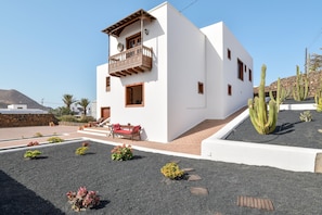 A modern white building with a balcony, a red bench, and cacti in the garden.